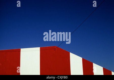 Detail der Spitze des Gebäudes gemalt mit breiten roten und weißen Bändern unter tiefblauem Himmel mit Telefon-Draht Stockfoto