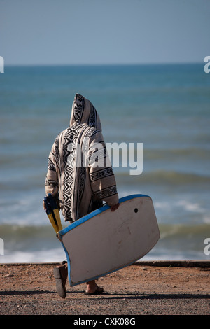 Mann in wollene Pullover mit Flossen und Bodyboard auf dem Seeweg, Marokko Stockfoto