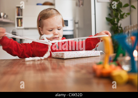 Kleines Mädchen sitzt am Tisch Geschenk auspacken Stockfoto