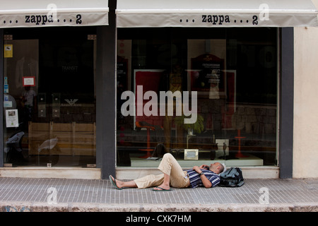 Ein einsamer Mann hinlegt und Gespräche über sein Handy außerhalb Ladengeschäft geschlossen während der Siesta-Zeit in Sitges, Spanien. Stockfoto