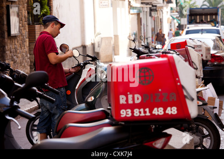 Ein junger Mann passt den Rückspiegel auf einem Motorrad für Pizza-Lieferservice in Sitges, Spanien verwendet. Stockfoto