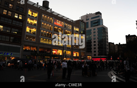 Twilight-Blick vom Union Square East, Menschen stehen Plaza Bürgersteig, elektrisches Licht Gebäude, East 14th Street, New York Stockfoto