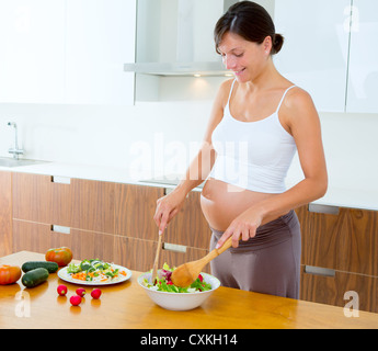 Schöne schwangere Frau in der Küche zu Hause vorbereiten Salat Stockfoto