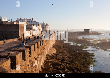 Menschen, die einen abendlichen Spaziergang entlang der Promenade am Sonnenuntergang in Essaouira, Marokko Stockfoto