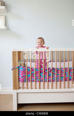 Babymädchen stehen in Krippe Stockfoto