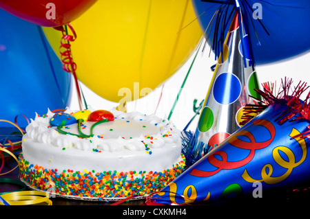 Einen weißen Geburtstagskuchen, umgeben von bunten Partyhüte und Band-Streamer Stockfoto