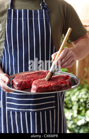 Mann Bürsten Steaks mit Olivenöl Stockfoto