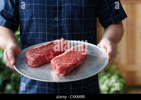 Mann hält Tablett mit rohen Steaks Stockfoto