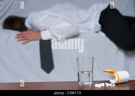 Glas Wasser und Pillen auf dem Tisch. Konzentrieren Sie im Hintergrund von einem übergebenen, Geschäftsmann auf dem Sofa. Stockfoto