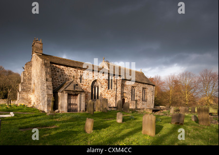 Die Außenseite des historischen sonnenbeschienenen Allerheiligen Kirche und Friedhof Grabsteine in ruhigen malerischen Landschaft unter dunklen Himmel, Weston, North Yorkshire, England, Großbritannien Stockfoto