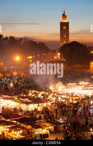 Marktstände und Menschen in der Abenddämmerung in Fna Jamaa el Fna Platz mit Souk Koutoubia-Minarett-Moschee Stockfoto