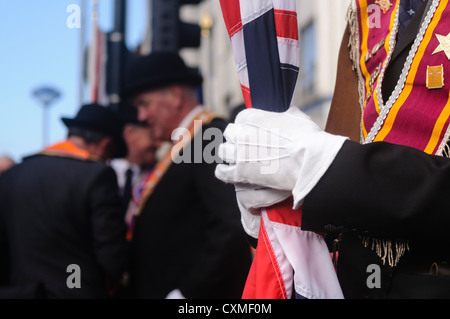 Orangeman mit weißen Handschuhen hält eine furled Anschluß-Markierungsfahne Stockfoto