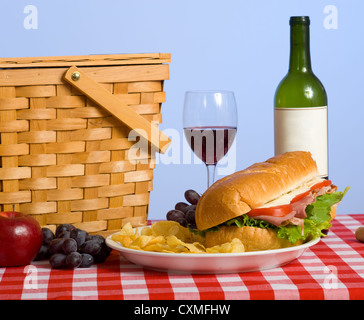 Ein Picknick-Mittagessen, bestehend aus einem Sandwich, Kartoffelchips, Wein und Trauben auf eine rote karierte Tischdecke Stockfoto