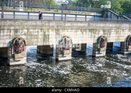 Frau geht über eine Fußgängerbrücke über das Wasser in Hannover, Deutschland mit geformten Fluss Gott Köpfe auf stützen. Stockfoto