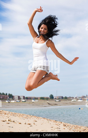 Junge Frau springt vor Freude, glücklich, aufgeregt am Strand im Sommer Stockfoto