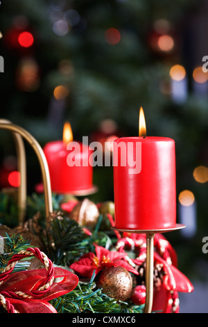 Adventskranz mit brennenden roten Kerzen, Weihnachtsbaum im Hintergrund Stockfoto