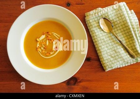 Roast Butternut-Kürbis-Suppe auf Holztisch in saubere weiße Schüssel mit Crème Fraiche und karamellisierten Samen garniert Stockfoto