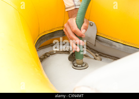Eine Nahaufnahme einer Person, die eine grüne Handpumpe greift und aktiv ein gelbes Schlauchboot aufpumpt. Die Pumpdüse wird mit einem Spiralseil in ein weißes Ventil auf dem Bootsboden eingeführt Stockfoto