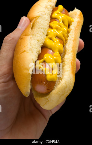 Hot Dog mit Senf in der Hand auf schwarzem Hintergrund Stockfoto
