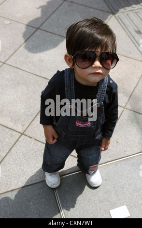 Es ist ein Foto von einem Kind oder Kind Junge mit Sonnenbrille. Er ist 2 Jahre alt und trage eine Jeans-Latzhose. Bild von oben oder höher Stockfoto