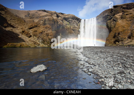 Die atemberaubenden Skogafoss Wasserfall in Island, mit Person unter einem bunten Wasserfall in den Schatten gestellt Stockfoto