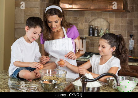 Ein attraktives Lächeln Familie der Mutter, zwei Kinder, Mädchen, junge, Sohn & Tochter, brechen Eiern & Backen in einer Küche zu Hause Stockfoto