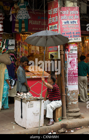 Mann verkaufte Änderung an einem Straßenrand stall unter einem schwarzen Regenschirm, vor Geschäften, Khari Baoli Straße (Markt Gewürzbasar aus Chandni Chowk), Alt-Delhi, Indien Stockfoto