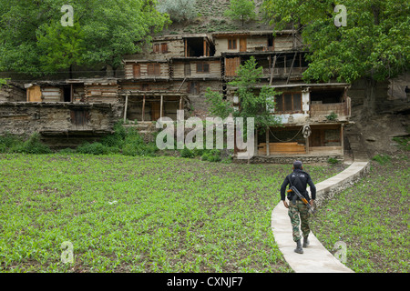 Bewaffnete Polizisten zu Fuß in Richtung steil terrassierte Häuser im Dorf Kalasha Grum, Rumbur Tal, Chitral, Khyber-Pakhtunkhwa, Pakistan Stockfoto