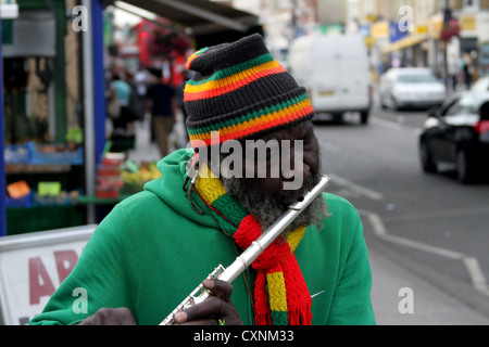 Spieler flutewise in London, in lebendige Rastafari-Farben tragen jamaikanische Flagge Fingerring, drei Vögelchen spielt Querflöte. Stockfoto