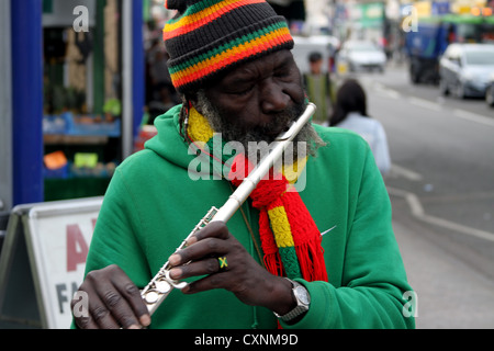 Spieler flutewise in London, in lebendige Rastafari-Farben tragen jamaikanische Flagge Fingerring, drei Vögelchen spielt Querflöte. Stockfoto