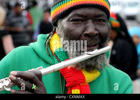 Rastafarischer Mann, der auf der Straße in london Flöte spielt, bekleidet, in lebhaften rastafaristischen Farben, mit Fingerring und Armbanduhr Stockfoto