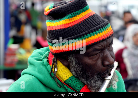 Spieler flutewise in London, in lebendige Rastafari-Farben tragen jamaikanische Flagge Fingerring, drei Vögelchen spielt Querflöte. Stockfoto