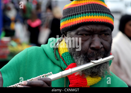 Spieler flutewise in London, in lebendige Rastafari-Farben tragen jamaikanische Flagge Fingerring, drei Vögelchen spielt Querflöte. Stockfoto