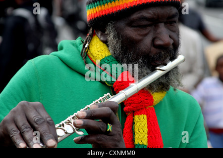 Spieler flutewise in London, in lebendige Rastafari-Farben tragen jamaikanische Flagge Fingerring, drei Vögelchen spielt Querflöte. Stockfoto