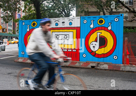 New York, NY - 7. Oktober 2012 Mann auf einem Fahrrad Reiten Vergangenheit eine Wandbild Müll bedeckt Müllcontainer im East Village. Stockfoto