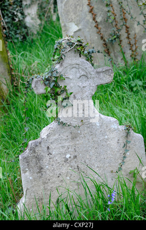 Ein Alter Stein Grabstein Kreuz mit Efeu bedeckt, auf einem grasbewachsenen Friedhof Stockfoto