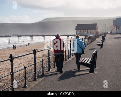 Ein Ehepaar im Ruhestand genießen warme Herbstsonne Bummeln auf der menschenleeren Promenade am Saltburn Stockfoto