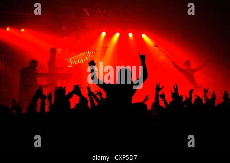 Silhouetted Zuschauer/Masse und Ambiente während live Rock Konzert mit Rocker auf der Bühne durch rote Strahler beleuchtet Stockfoto