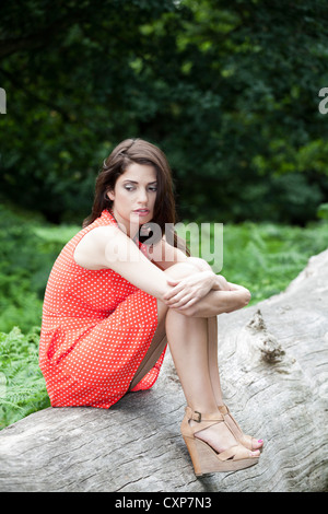 Junge Frau sitzt auf dem Baumstamm denken Stockfoto