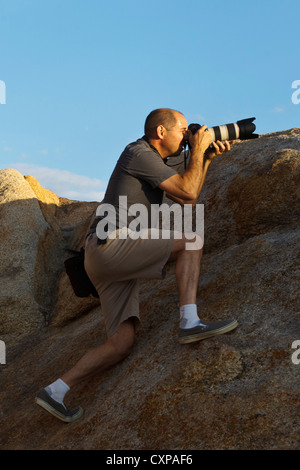 Fotograf mit Teleobjektiv stehend auf einem großen Felsen, Alabama Hills, Lone Pine, Kalifornien, Vereinigte Staaten von Amerika Stockfoto