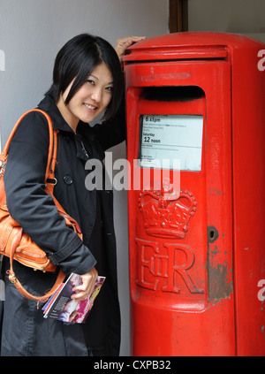 Junge Japanerin Posten Briefe in traditionellen rot Royal Mail-Briefkasten, Stratford-upon-Avon, Warwickshire, England, UK Stockfoto