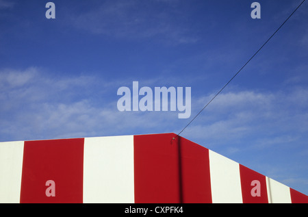 Detail der Spitze des Gebäudes gemalt mit breiten roten und weißen Bändern unter blauem Himmel mit Telefon-Draht Stockfoto