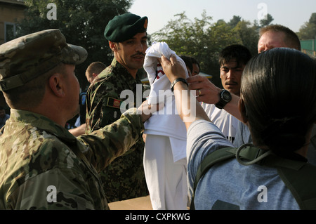 Afghan National Army Command Sgt. Maj. Muhebullah, Senior noncommissioned Officer der ANA Armee unterstützt den Befehl, Hände, die T-Shirts zu seinen Soldaten, die eingeladen wurden, in der Armee 10 teilzunehmen - miler Schatten beim Camp Eggers, Kabul, Afghanistan Okt. 7. Einige der ANA Soldaten kamen aus Randgebieten und wurden von ihren Einheiten ausgewählt, sie für den Fall zu vertreten. Sieben der acht Teilnehmer durchgeführt, die in weniger als 78 Minuten. Die ANA war durch ihre Logistik Mentoren und Trainer eingeladen, im Vorfeld zu beteiligen, als tem Gebäude auch von Art. Stockfoto