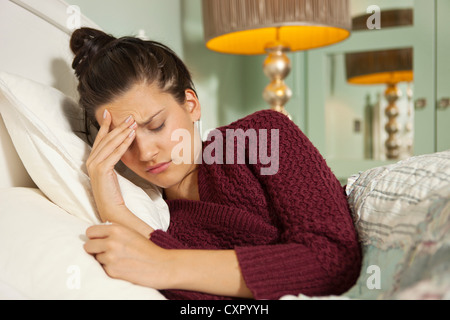 Junge Frau im Bett mit Kopfschmerzen Stockfoto