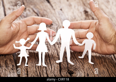 Pappfiguren der Familie auf einem Holztisch. Das Symbol der Einheit und des Glücks. Händen umarmen sanft die Familie. Stockfoto