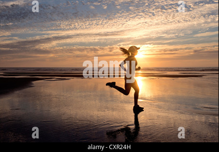 Frau läuft am Strand bei Sonnenaufgang Stockfoto