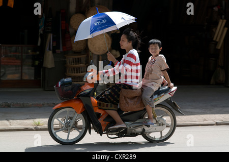 Eine Mutter und ihr Sohn passieren auf ihrem Motorrad in Luang Prabang, Laos Stockfoto