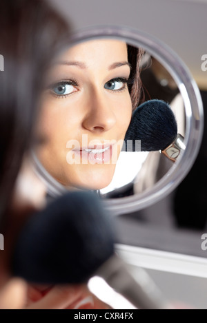 Junge Frau bei einem Schminktisch hält einen Handspiegel und einem Puderpinsel Stockfoto