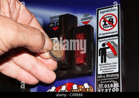 Die Hand eines Mannes ist eine Euro-Münze einfügen in ein Spielautomat, Warnschild, Spielsucht Stockfoto