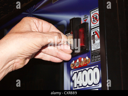 Die Hand eines Mannes ist eine Euro-Münze einfügen in ein Spielautomat, Warnschild, Spielsucht Stockfoto